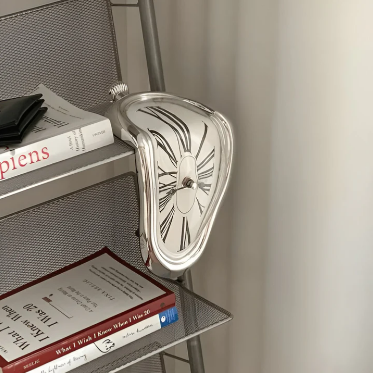 Silver surrealist melting clock resting on the edge of a metal bookshelf next to books