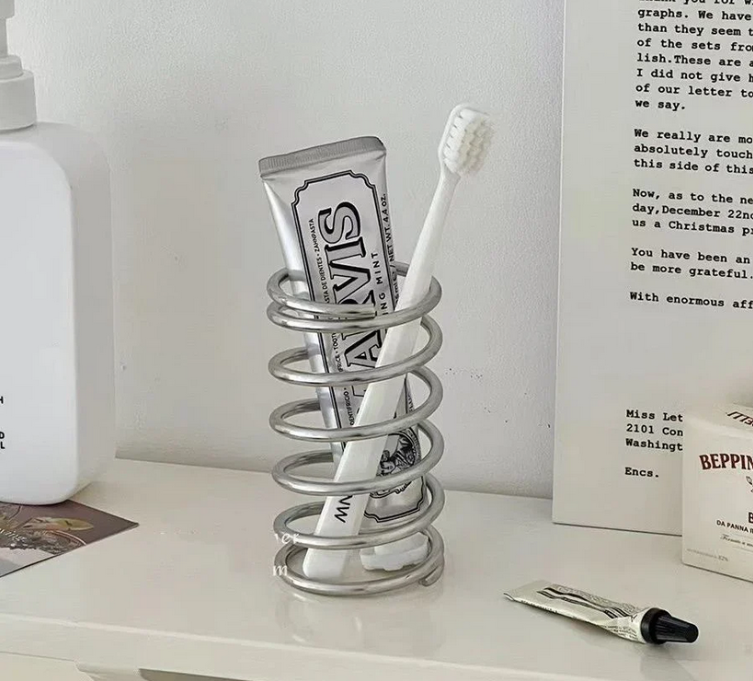 Silver chrome spiral toothbrush holder on white bathroom sink with luxury toothpaste